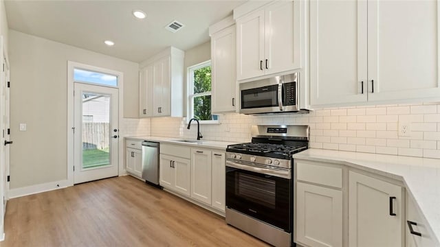 1209 SW Journey Ln, Bentonville, AR 72713 - kitchen with stainless steel appliances, light wood-style flooring, backsplash, white cabinetry, and light stone counters