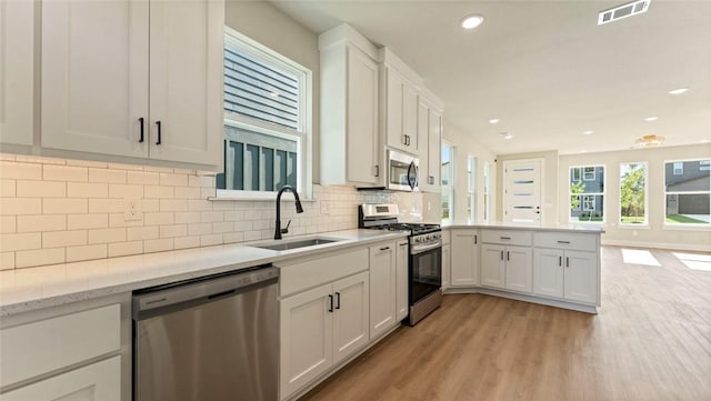 1209 SW Journey Ln, Bentonville, AR 72713 - kitchen featuring appliances with stainless steel finishes, a peninsula, light wood-style floors, tasteful backsplash, and white cabinetry
