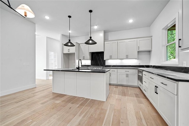 1421 Lee St, Pea Ridge, AR 72751 - kitchen with dark countertops, light wood-type flooring, white cabinets, a kitchen island with sink, and tasteful backsplash