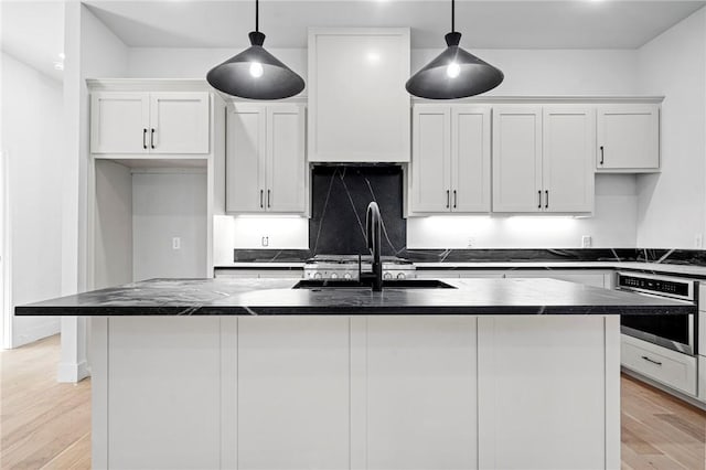 1421 Lee St, Pea Ridge, AR 72751 - kitchen with oven, a kitchen island with sink, dark countertops, and light wood-style floors