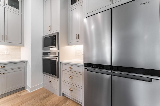 6741 Garden Trail Ave, Springdale, AR 72762 - kitchen with stainless steel appliances, light wood-style flooring, decorative backsplash, light countertops, and glass insert cabinets