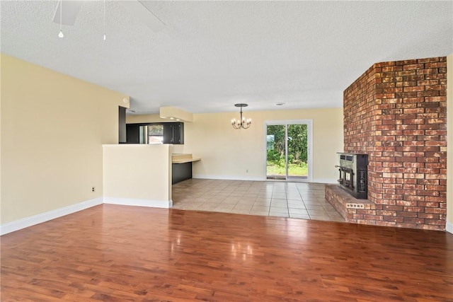 50233 S 725th Rd, Colcord, OK 74338 - unfurnished living room featuring wood finished floors, a chandelier, a brick fireplace, a textured ceiling, and a ceiling fan