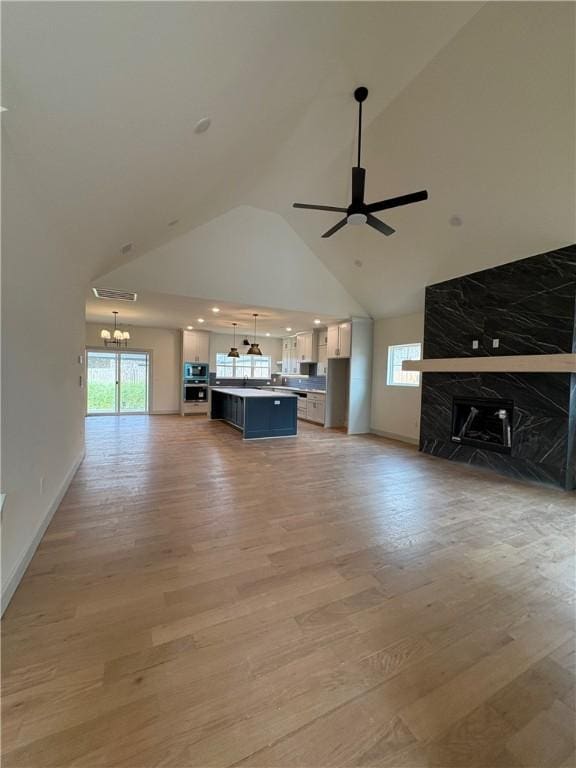 1309 Carrara, Tontitown, AR 72762 - unfurnished living room featuring a chandelier, a ceiling fan, high vaulted ceiling, light wood finished floors, and healthy amount of natural light