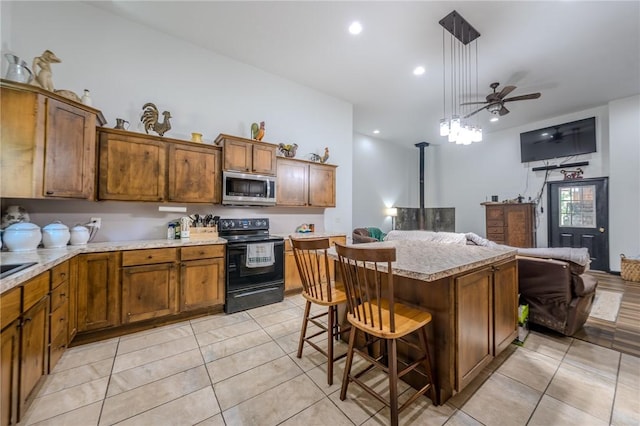 19959 Rheas Community Rd, Lincoln, AR 72744 - kitchen featuring stainless steel microwave, black electric range oven, brown cabinets, light countertops, and a wood stove