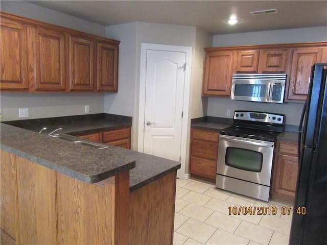 1110 Courage, Siloam Springs, AR 72761 - kitchen with stainless steel appliances, dark countertops, light tile patterned floors, brown cabinets, and recessed lighting