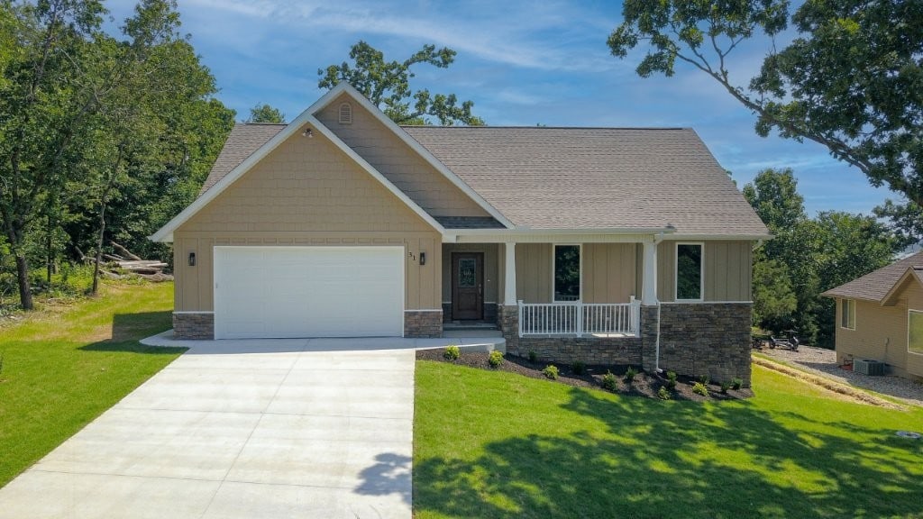 31 Dunkeld Dr, Bella Vista, AR 72715 - craftsman-style home featuring a garage, a porch, driveway, stone siding, and a front lawn