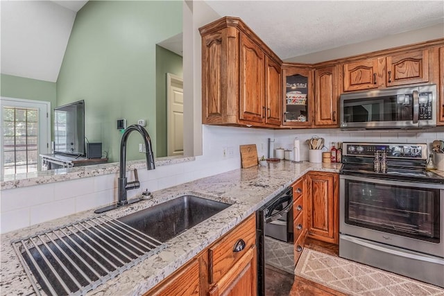 3 Jared Ln, Conway, AR 72032 - kitchen featuring appliances with stainless steel finishes, brown cabinetry, light stone counters, lofted ceiling, and backsplash