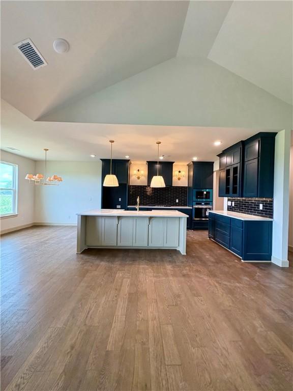 825 Bellagiola, Tontitown, AR 72762 - kitchen with light countertops, a chandelier, wood finished floors, backsplash, and a large island with sink