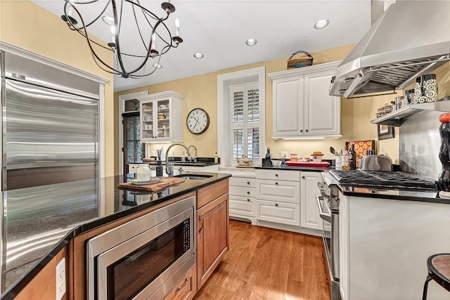 32 Armstrong St, Eureka Springs, AR 72632 - kitchen featuring wall chimney exhaust hood, built in appliances, white cabinets, light wood-type flooring, and recessed lighting