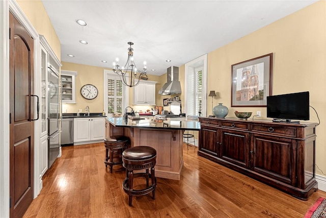 32 Armstrong St, Eureka Springs, AR 72632 - kitchen with wall chimney exhaust hood, dark wood finished floors, dark countertops, an island with sink, and recessed lighting