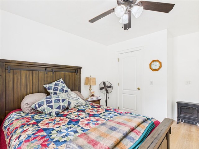 104 Paradise Cove Ln, Berryville, AR 72616 - bedroom featuring a wood stove, light wood-type flooring, and a ceiling fan