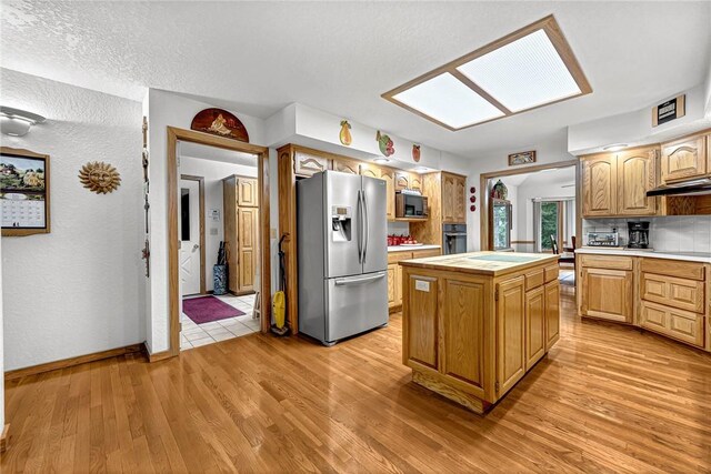 8553 Stoner Ln, Rogers, AR 72756 - kitchen with stainless steel fridge, light countertops, light wood finished floors, a kitchen island, and under cabinet range hood