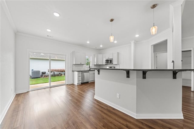 2 Wendike Ln, Bella Vista, AR 72715 - kitchen featuring appliances with stainless steel finishes, dark countertops, a breakfast bar, ornamental molding, and dark wood finished floors