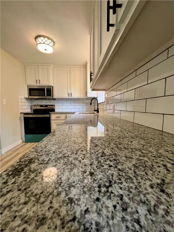 3501 Pleasant, Ozark, AR 72949 - kitchen featuring electric range, stainless steel microwave, stone countertops, backsplash, and white cabinets