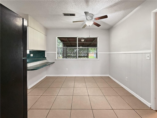 1906 S W End St, Springdale, AR 72764 - unfurnished dining area featuring a ceiling fan, a textured ceiling, light tile patterned floors, and a wainscoted wall