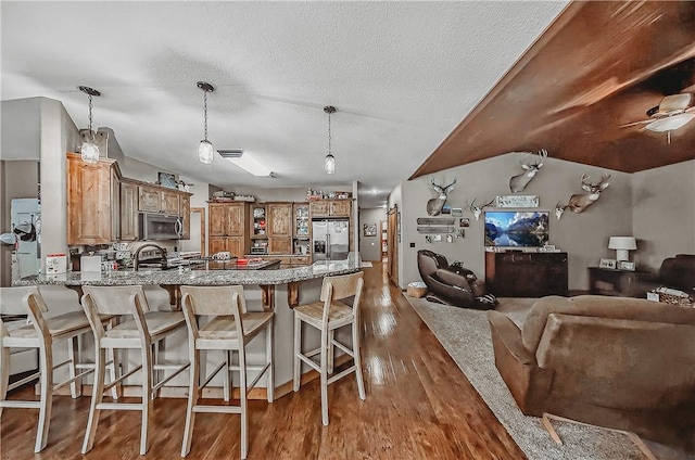 19123 Nokes Farm Rd, Siloam Springs, AR 72761 - kitchen featuring appliances with stainless steel finishes, a peninsula, wood finished floors, brown cabinetry, and light stone counters