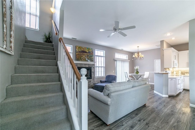 6682 Firefly Catch Ave, Springdale, AR 72762 - living room featuring stairway, dark wood-type flooring, a chandelier, ceiling fan, and a stone fireplace