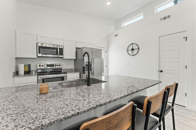 671 St Charles Pl, Bentonville, AR 72713 - kitchen with stainless steel appliances, a breakfast bar area, light stone countertops, light wood-type flooring, and a towering ceiling