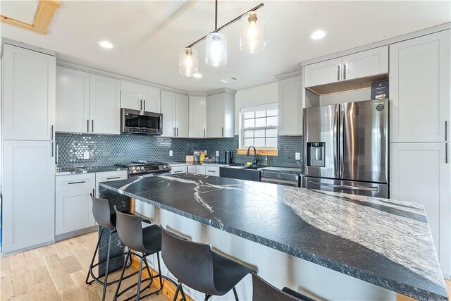 11 Darian Dr, Bentonville, AR 72712 - kitchen featuring stainless steel appliances, decorative backsplash, a kitchen breakfast bar, light wood-type flooring, and decorative light fixtures