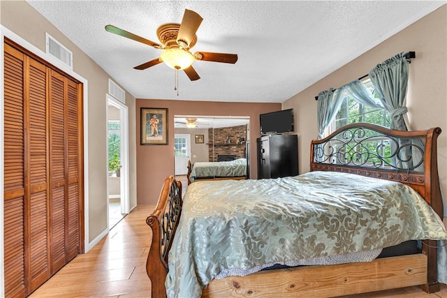594 Madison 8650, Huntsville, AR 72740 - bedroom with light wood-style floors, a closet, a fireplace, a textured ceiling, and a ceiling fan