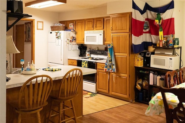 1013 N 26th St, Rogers, AR 72756 - kitchen featuring white appliances, brown cabinetry, light countertops, light wood-style flooring, and a kitchen bar