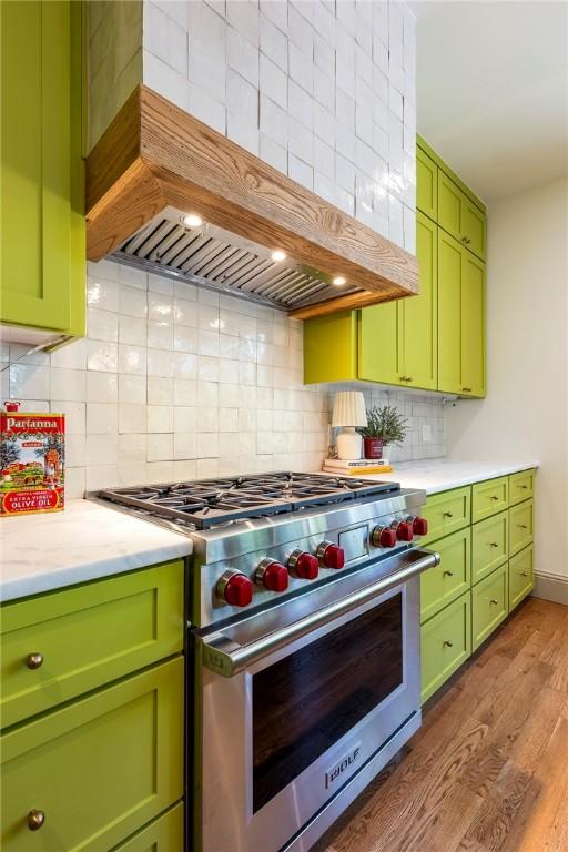 300 NW 5th St, Bentonville, AR 72712 - kitchen featuring designer stove, premium range hood, green cabinetry, wood finished floors, and backsplash