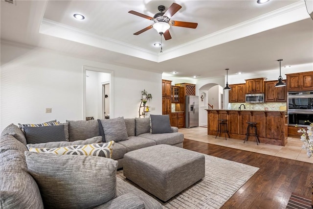 5100 SW Blaire Mont Rd, Bentonville, AR 72713 - living area with a tray ceiling, a ceiling fan, arched walkways, light wood finished floors, and crown molding