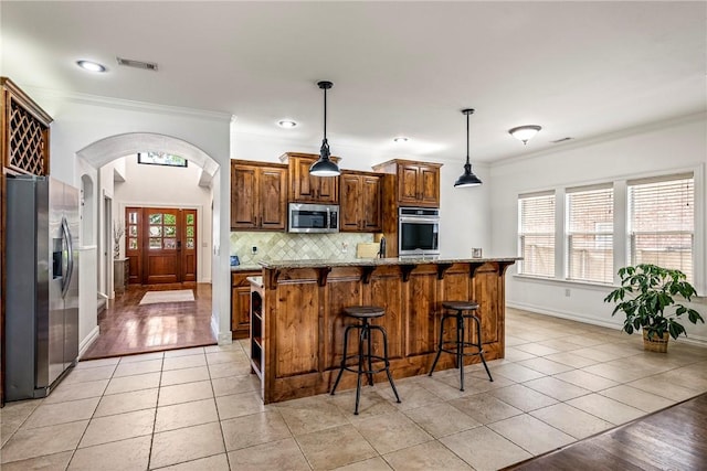 5100 SW Blaire Mont Rd, Bentonville, AR 72713 - kitchen featuring appliances with stainless steel finishes, crown molding, light tile patterned floors, arched walkways, and a breakfast bar area