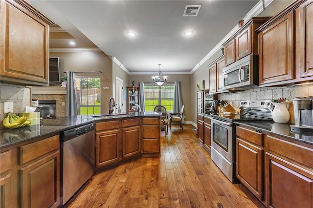 216 Windsor Ave, Lowell, AR 72745 - kitchen with stainless steel appliances, a chandelier, hardwood / wood-style flooring, decorative backsplash, and a fireplace