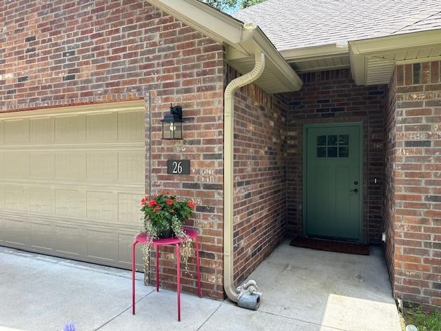 26 Osborne Dr, Bella Vista, AR 72715 - property entrance with brick siding, roof with shingles, and an attached garage