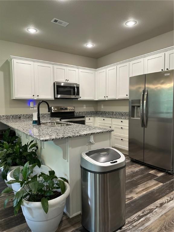 26 Osborne Dr, Bella Vista, AR 72715 - kitchen featuring appliances with stainless steel finishes, a peninsula, white cabinetry, dark wood-type flooring, and a kitchen bar