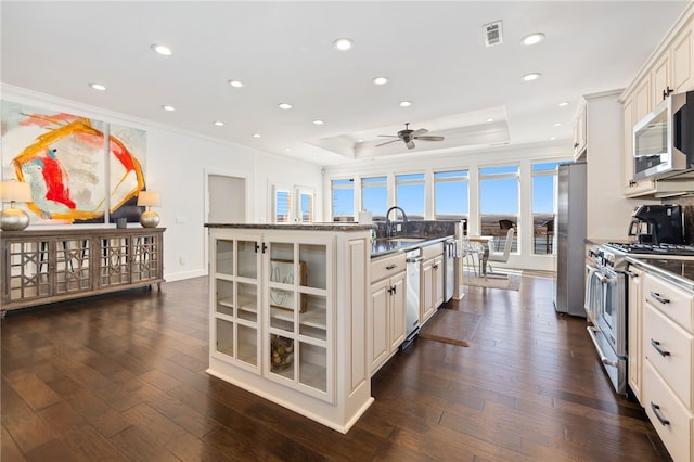 40 Rivercliff Rd, Rogers, AR 72756 - kitchen featuring appliances with stainless steel finishes, ornamental molding, glass insert cabinets, a kitchen island with sink, and a tray ceiling