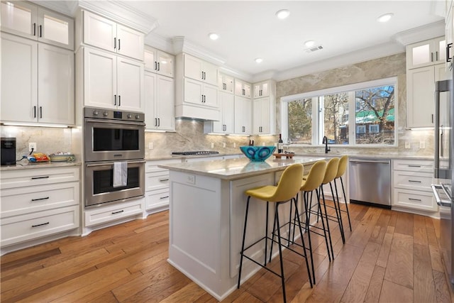 837-839 N Gregg Ave, Fayetteville, AR 72701 - kitchen featuring stainless steel appliances, decorative backsplash, light wood finished floors, a breakfast bar, and white cabinets