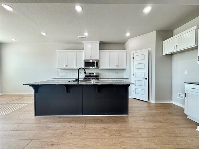 4807 SW Wakanda St, Bentonville, AR 72713 - kitchen with appliances with stainless steel finishes, tasteful backsplash, a breakfast bar, white cabinetry, and light wood finished floors