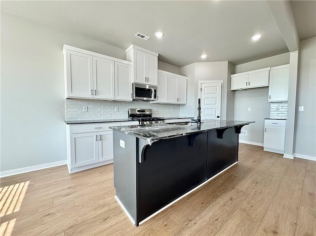 4807 SW Wakanda St, Bentonville, AR 72713 - kitchen with stainless steel appliances, decorative backsplash, light wood-type flooring, white cabinets, and recessed lighting