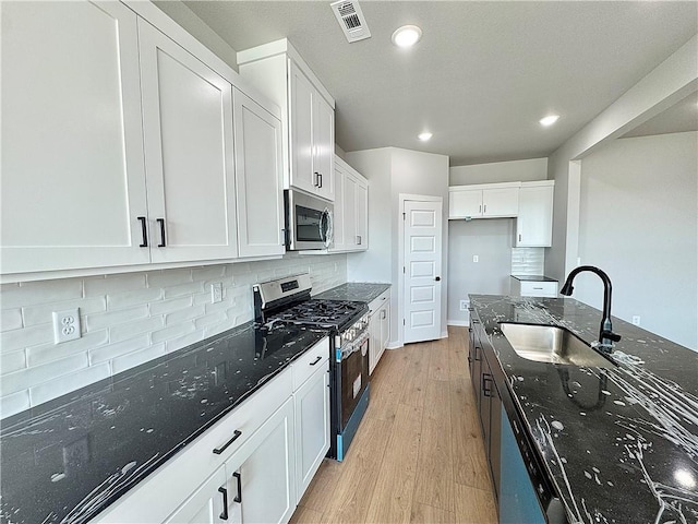 4807 SW Wakanda St, Bentonville, AR 72713 - kitchen featuring appliances with stainless steel finishes, light wood finished floors, dark stone countertops, decorative backsplash, and recessed lighting