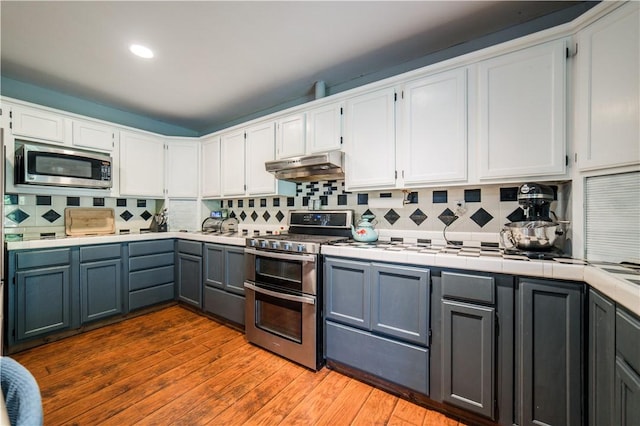 21569 Sibley Rd, Sulphur Springs, AR 72768 - kitchen with stainless steel appliances, under cabinet range hood, tile counters, white cabinetry, and recessed lighting