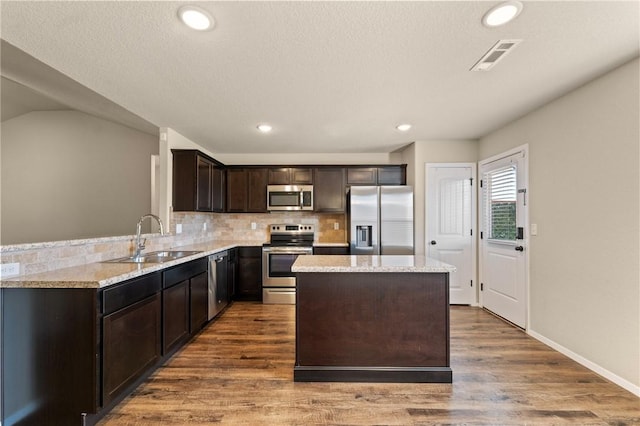 2504 Maplewood Ave, Lowell, AR 72745 - kitchen with appliances with stainless steel finishes, dark brown cabinetry, wood finished floors, a kitchen island, and tasteful backsplash