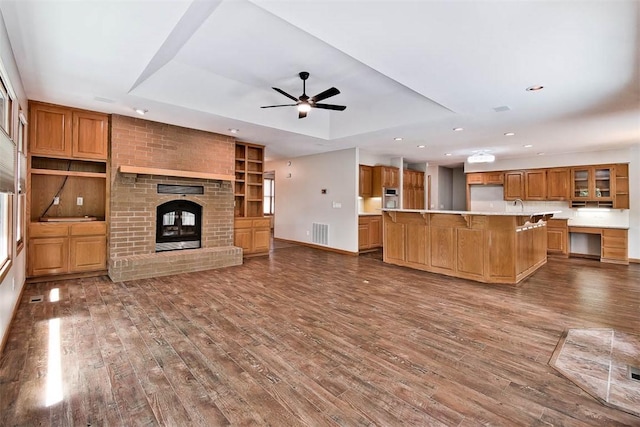 1 May Ln, Bella Vista, AR 72715 - unfurnished living room featuring dark wood finished floors, ceiling fan, a fireplace, recessed lighting, and a tray ceiling