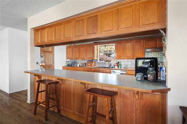 13183 Shady Grove Rd, Gravette, AR 72736 - kitchen featuring brown cabinets, dark wood-style floors, dishwasher, backsplash, and a textured ceiling