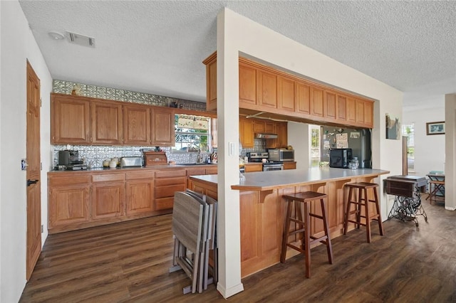 13183 Shady Grove Rd, Gravette, AR 72736 - kitchen featuring appliances with stainless steel finishes, dark wood-type flooring, a textured ceiling, backsplash, and a breakfast bar area