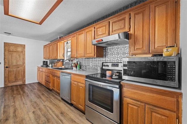 13183 Shady Grove Rd, Gravette, AR 72736 - kitchen with appliances with stainless steel finishes, under cabinet range hood, backsplash, light wood finished floors, and a textured ceiling