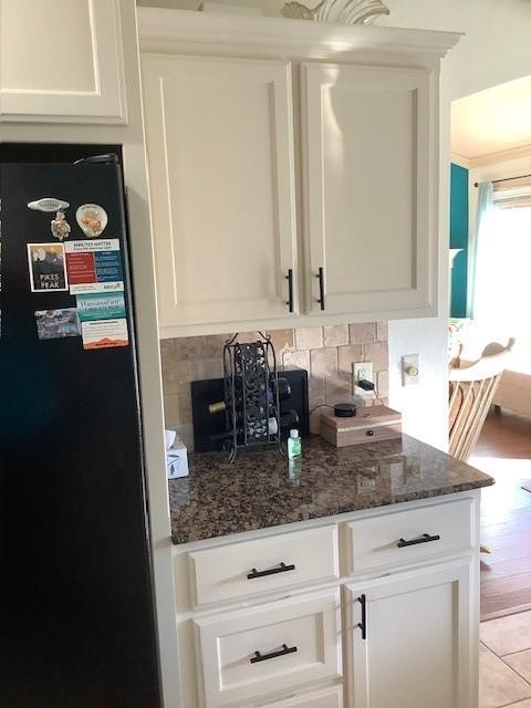 3809 N 2nd Pl, Rogers, AR 72756 - kitchen with freestanding refrigerator, decorative backsplash, dark stone counters, and white cabinetry