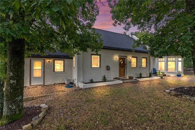 393 Timberlake Ln, Eureka Springs, AR 72631 - back of property at dusk featuring stucco siding, a chimney, and roof with shingles