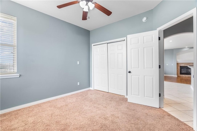 13449 Loyle Ln, Gravette, AR 72736 - unfurnished bedroom featuring arched walkways, a closet, light colored carpet, a tile fireplace, and light tile patterned flooring
