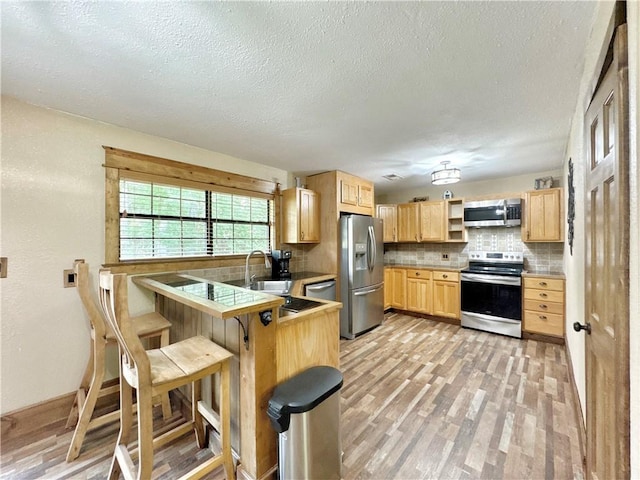 8500 Rock Creek Rd, Mulberry, AR 72947 - kitchen featuring stainless steel appliances, light brown cabinets, tasteful backsplash, a textured ceiling, and a breakfast bar area