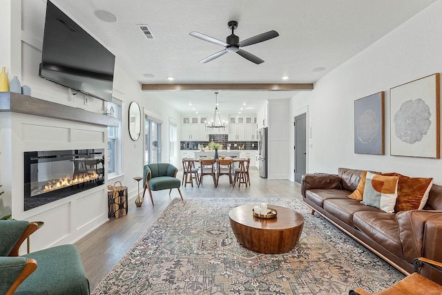 103 NW Ozark Way, Bentonville, AR 72712 - living room featuring light wood-style floors, a ceiling fan, a glass covered fireplace, a chandelier, and a textured ceiling
