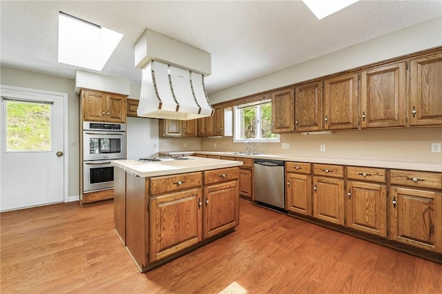8394 Admiral Nimitz Dr, Rogers, AR 72756 - kitchen featuring appliances with stainless steel finishes, brown cabinetry, light wood-type flooring, light countertops, and custom range hood