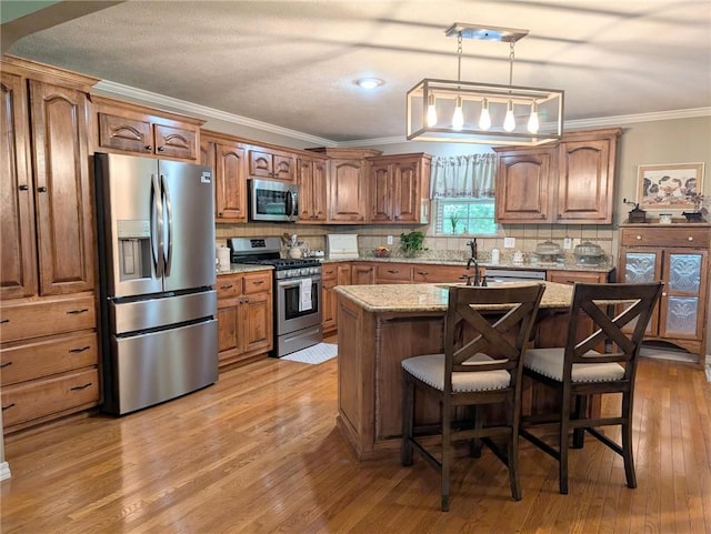 1445 Woodhaven Ln, Harrison, AR 72601 - kitchen with appliances with stainless steel finishes, ornamental molding, light wood-type flooring, light stone counters, and a kitchen island with sink