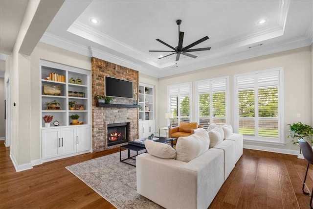 1200 Birkshire Cir, Cave Springs, AR 72718 - living room with a raised ceiling, a ceiling fan, ornamental molding, a brick fireplace, and dark wood-style flooring